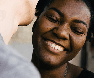 A woman smiles happily toward the viewer, hugging a man.