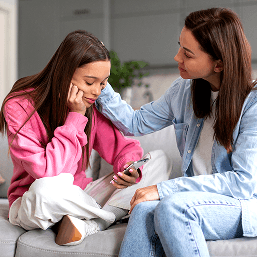 A mother comforts a teenaged girl as she looks down at her phone